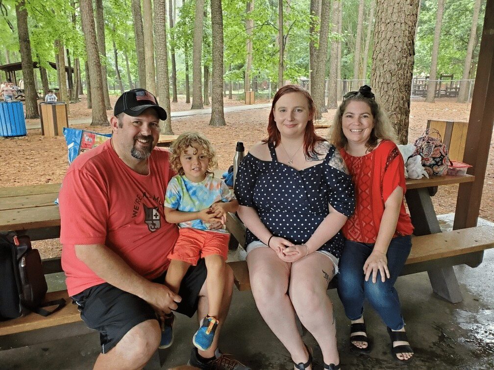 Birth mother, adoptee, and adoptive parents sitting on picnic table together.