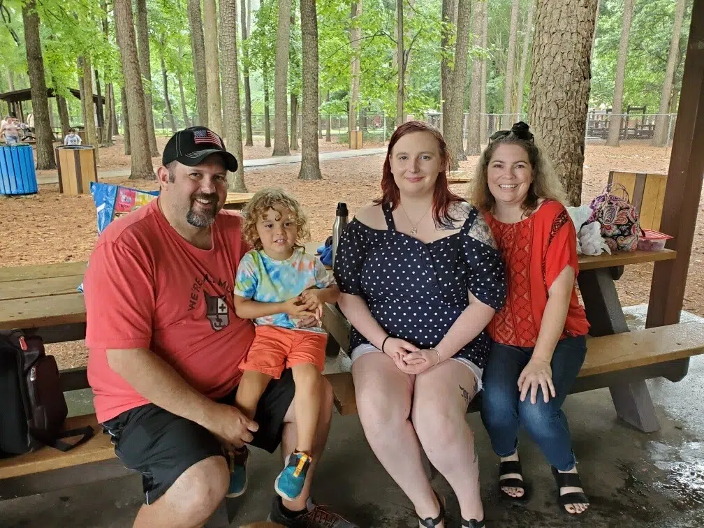 Birth mother, adoptee, and adoptive parents sitting on picnic table together.